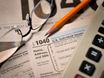 Close-up of a U.S. tax form 1040 with glasses, a pencil, and a calculator.