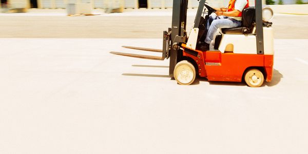Man operating a forklift in an industrial area under a blue sky.