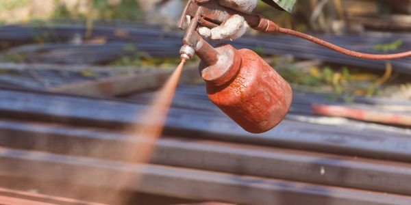 Hand spraying rust protector on steel rods at a construction site.