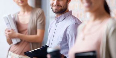 Three young professionals standing and smiling, holding work materials.