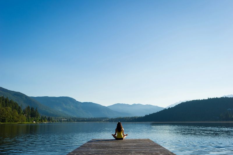 Female meditating doing sukhasana or Easy Pose during a yoga working at a pristine mountain lake