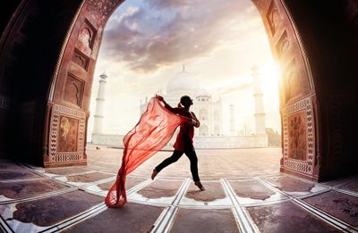 Silhouette of a woman running with a flowing red scarf at the Taj Mahal entrance.
