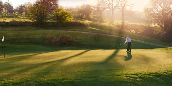 A golfer putting on a green during sunset.
