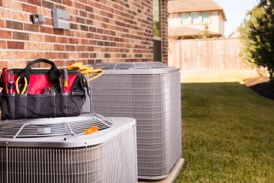 HVAC units outside a brick house with a tool bag on top.
