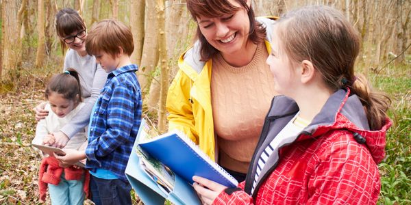 Group of children and adults exploring nature with notebooks.