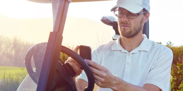 Man in golf cart on the course effortlessly managing tee times with friends on the TeeMeUp app. 