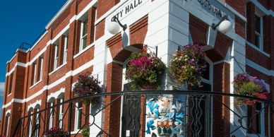 Flower pots adorn the corner of a red and white city hall building under a clear blue sky.