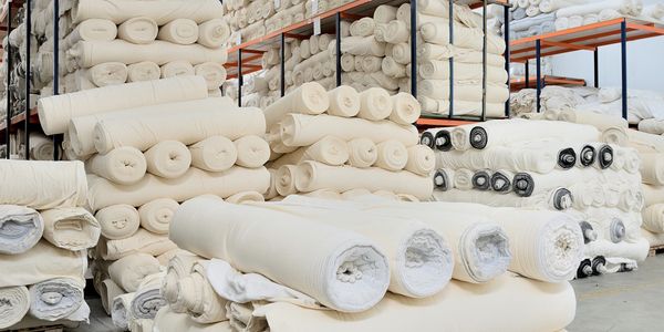Stacks of rolled white fabric arranged in a storage warehouse.