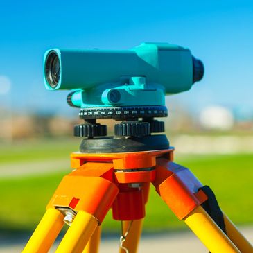 Surveying instrument on an orange tripod outdoors.