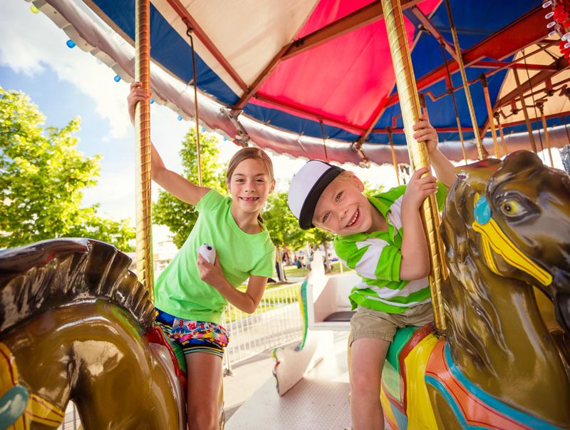 Two cute kids enjoying a ride on a fun carnival carousel. A happy girl and boy are Smiling and having fun together at the summer carnival