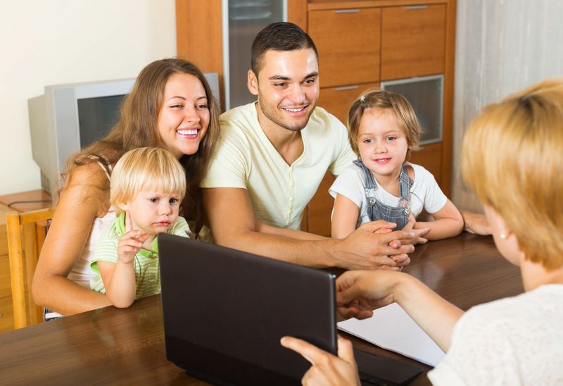 Insurance agent consulting smiling young family with kids at home. Focus on woman