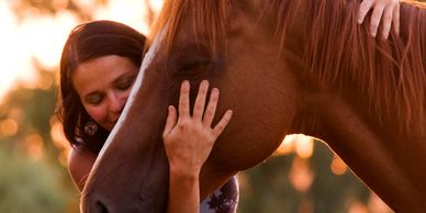 A woman gently embraces a brown horse at sunset.