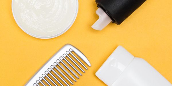 Hair care products including a comb, cream, and lotion on a yellow background.