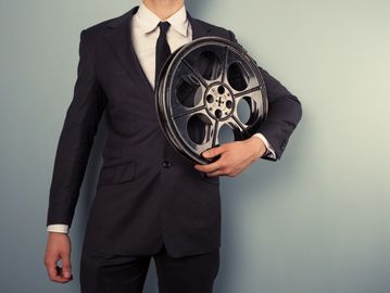 Man in suit holding a film reel against a plain background.