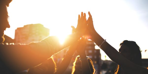 Group of people doing a high-five at sunset outdoors.