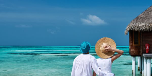 Couple sitting on a wooden deck by turquoise sea under a clear blue sky.