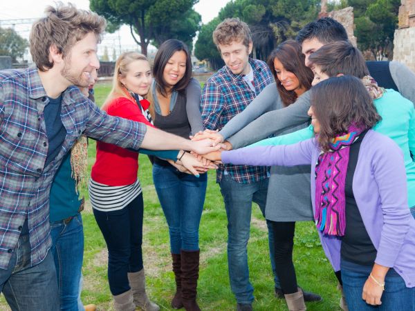 Group of friends putting their hands together in a huddle outdoors.