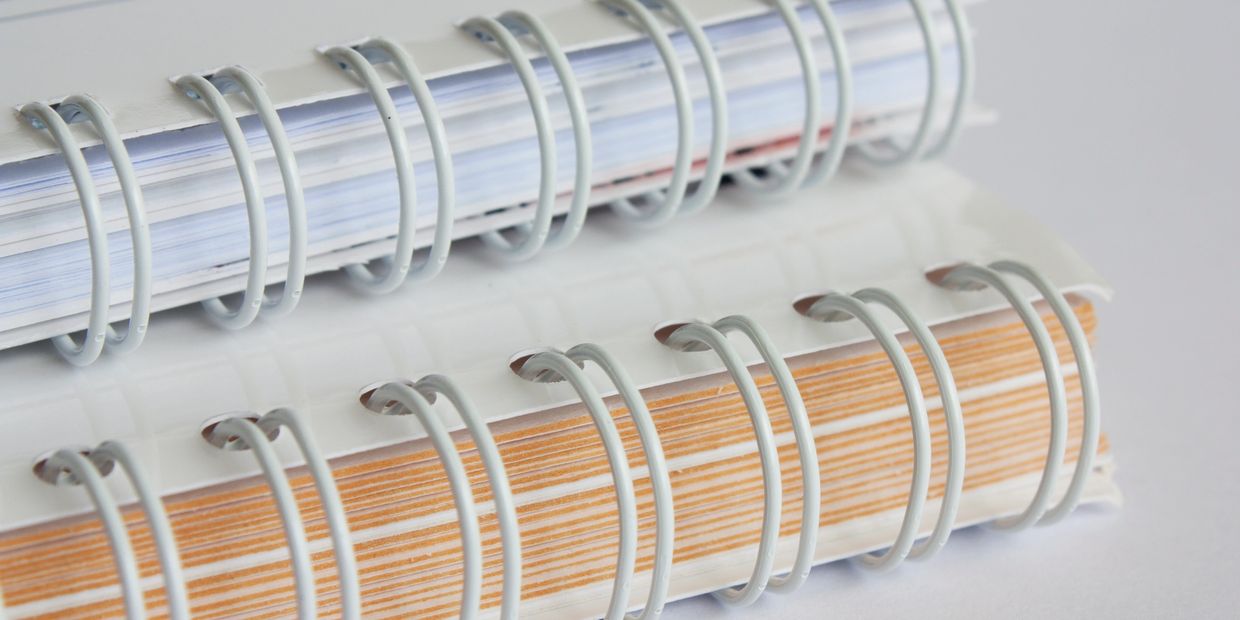 Close-up of two white spiral-bound notebooks stacked on a white surface.