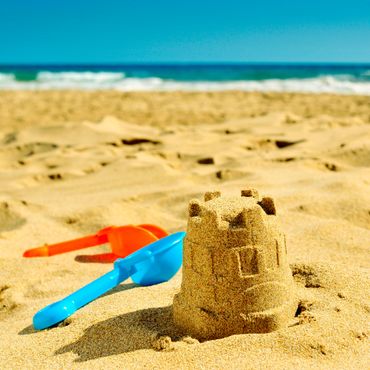 A small sandcastle with colorful plastic shovels on a sunny beach.