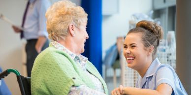Young nurse smiling at elderly woman in wheelchair.