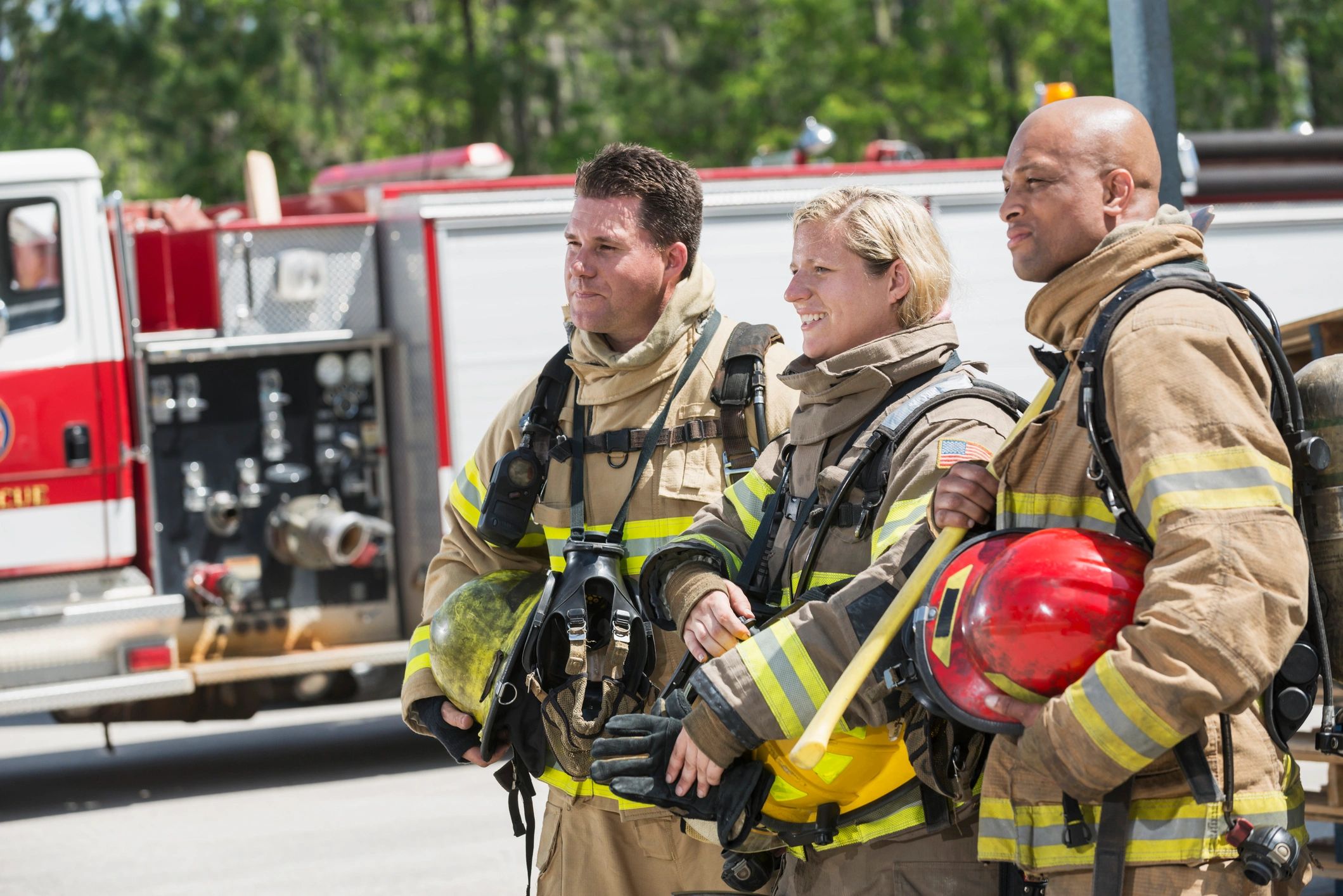 Three firefighters in full gear stand together near a fire truck.