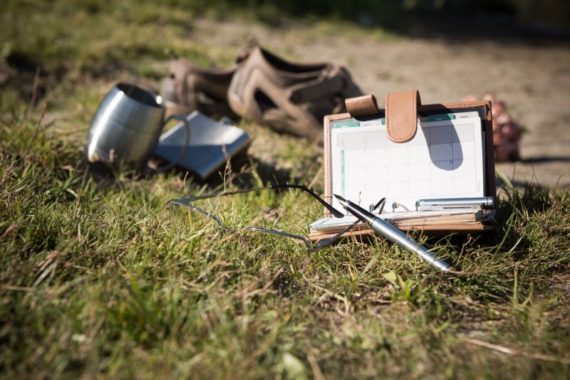 Writing pad, fountain pen, steel flack and mug, men's sandals and glasses on meadow grass near the river.