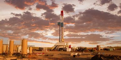 Oil drilling rig at sunset with dramatic clouds.