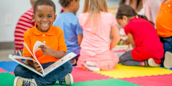 Smiling boy reading a book on a colorful mat.