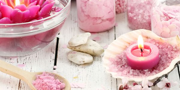 Pink spa essentials with candle, bath salts, and stones on wooden table.
