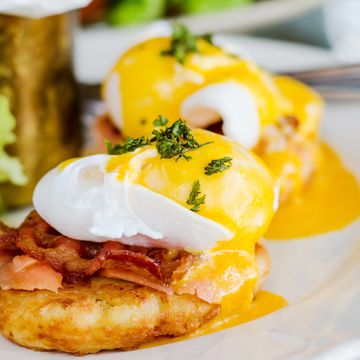 Close-up of eggs Benedict with poached eggs, bacon, and hollandaise sauce on a crispy base.
