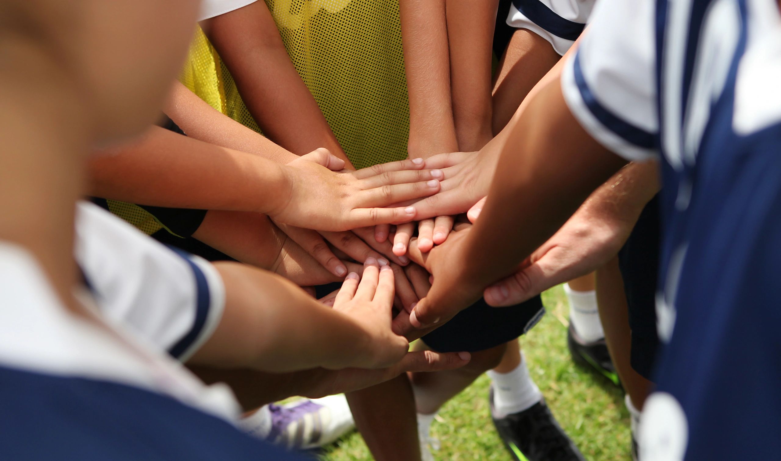 Young athletes stacking hands in a team huddle outdoors.