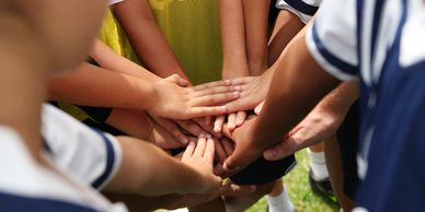 Young athletes join hands in a team huddle symbolizing unity and teamwork.