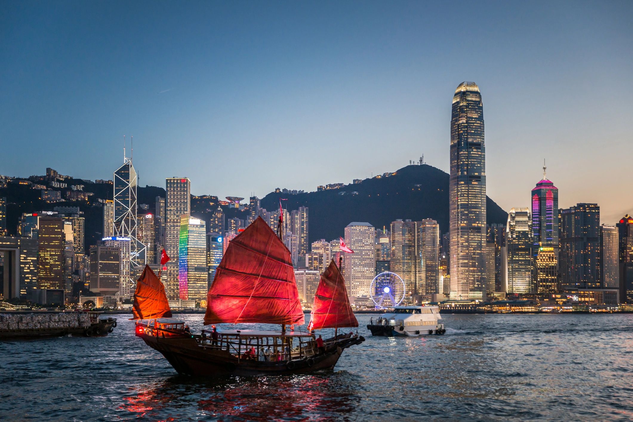 Traditional sailboats with city skyline at dusk.