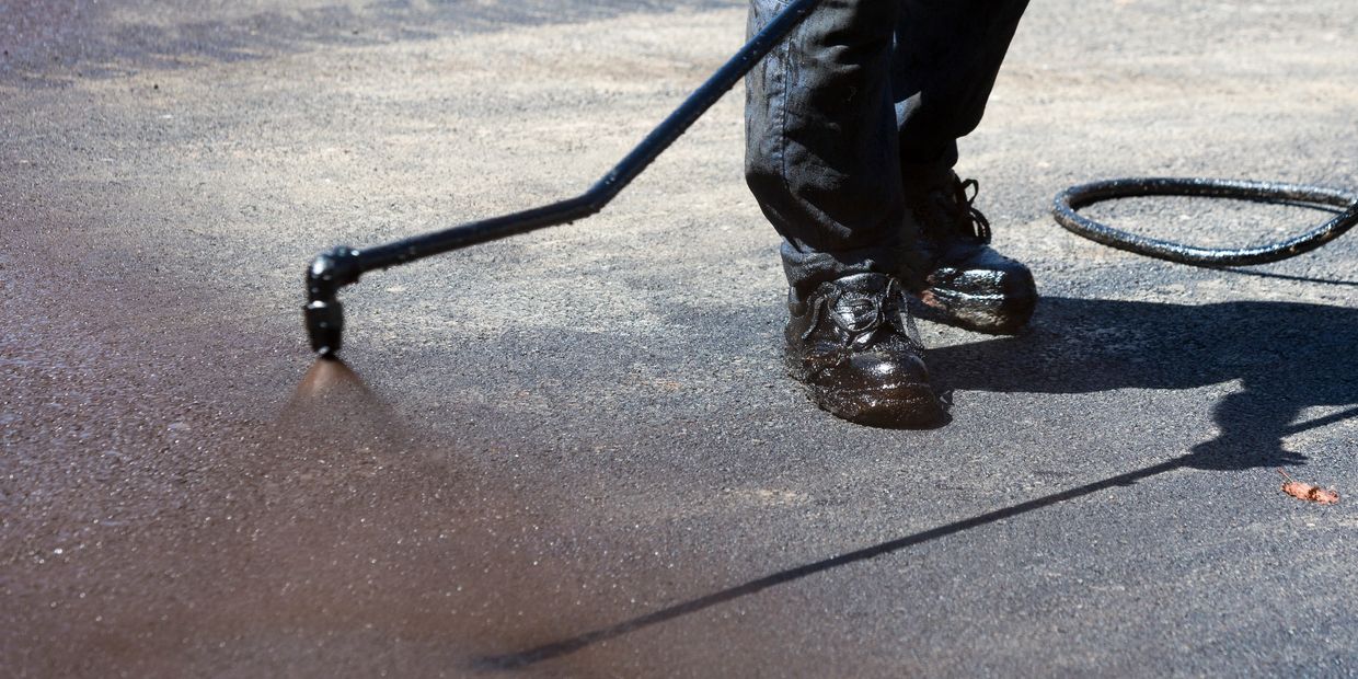 Person applying a sealant on pavement with protective boots.