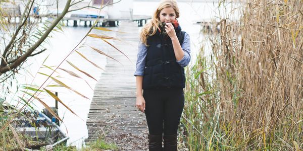 Woman standing on a wooden dock by the water, surrounded by tall reeds.