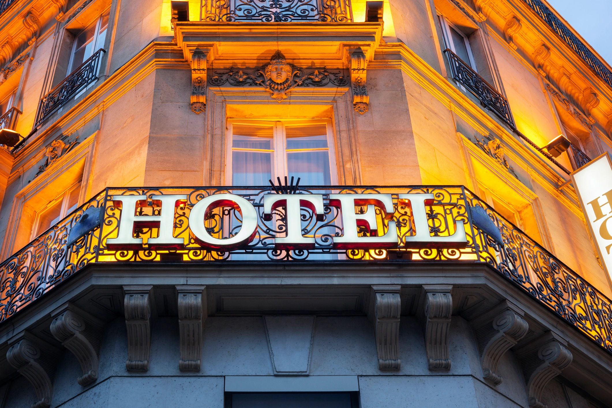 Illuminated hotel sign on ornate balcony.
