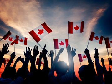 Silhouettes of people waving Canadian flags at sunset.