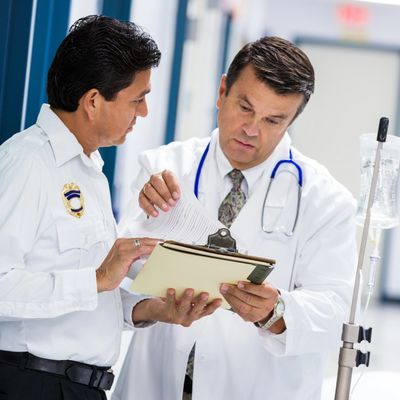 Doctor explaining medical documents to a security officer in hospital corridor.