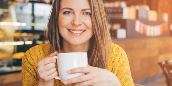 Smiling woman enjoying a warm drink in a cozy cafe.