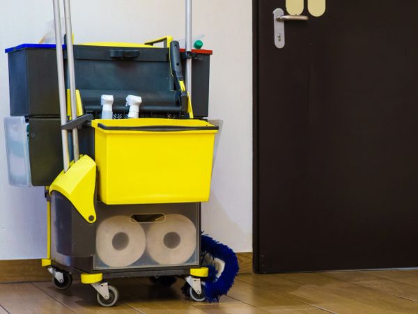 A yellow and black janitorial cart with cleaning supplies near a restroom door.
