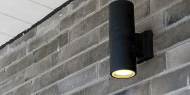 Modern black outdoor wall light mounted on a gray brick wall.