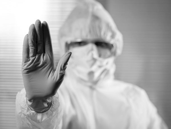 Person in protective suit and gloves showing a stop gesture.