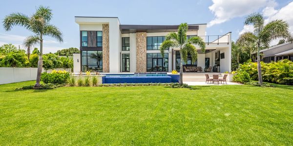 Modern house with large glass windows, pool, and lush green lawn.