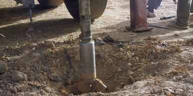 A close-up of a large metal drill digging into the ground with people nearby.