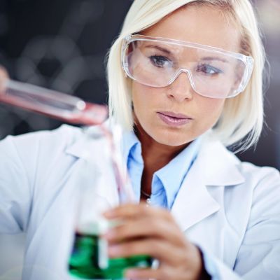 Female scientist wearing safety goggles pouring liquid in a lab.
