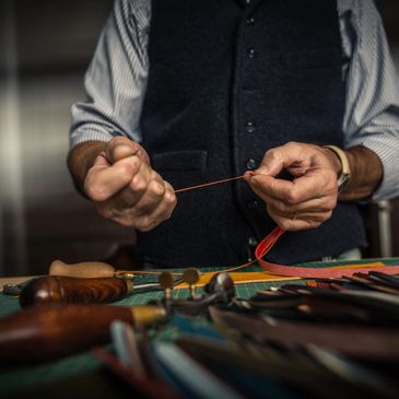 Craftsman stretching thread for leatherwork with tools on a worktable.