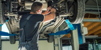 Mechanic repairing car underside on hydraulic lift in workshop.