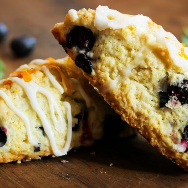 Close-up of blueberry scones with icing on a wooden surface.