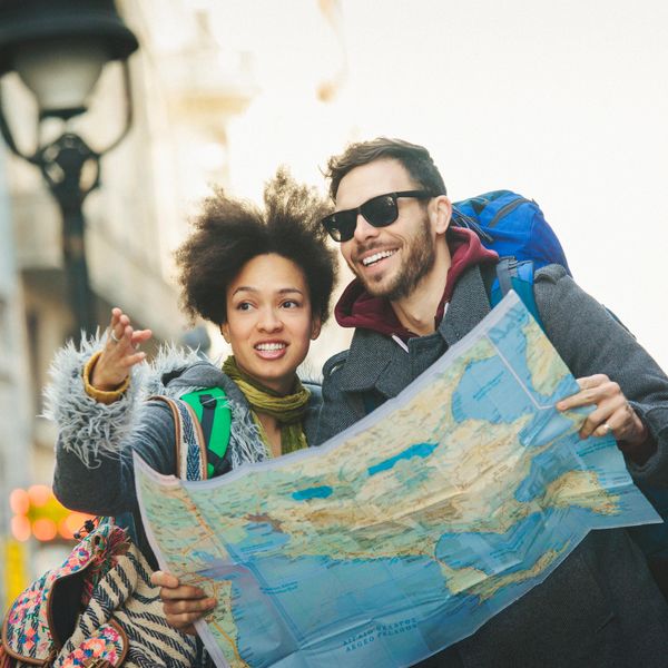 Couple with backpacks looking at a map while exploring a city.