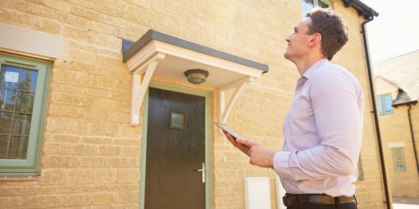 Man inspecting a house exterior with a tablet in hand.